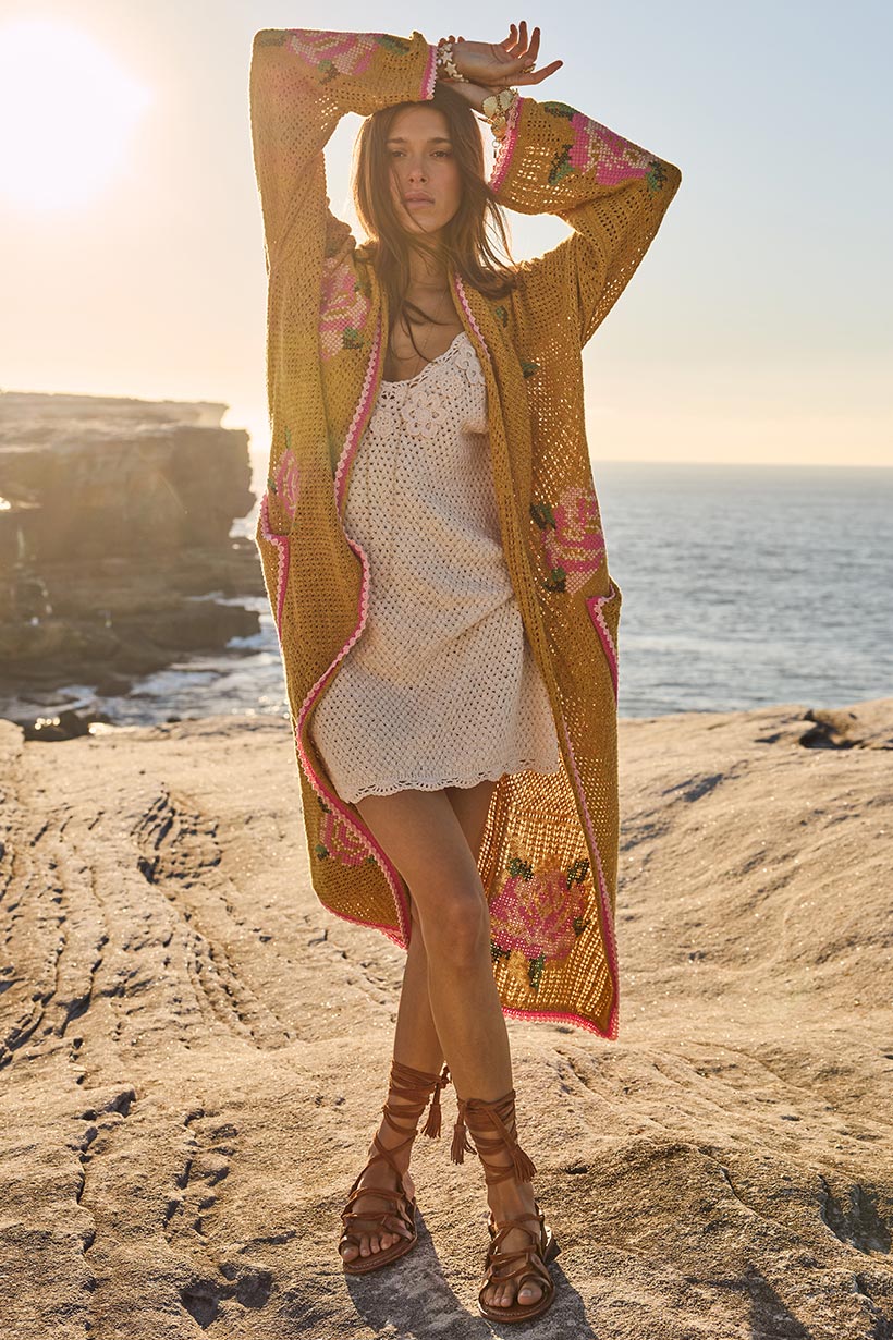 Woman in a long, patterned cardigan over a white dress standing on a rocky beach with ocean and sunset in the background.
Coastal Granny Maxi Cardigan