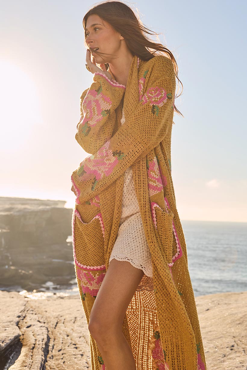 Woman in a long, patterned cardigan over a white dress standing on a rocky beach with ocean and sunset in the background.
Coastal Granny Maxi Cardigan