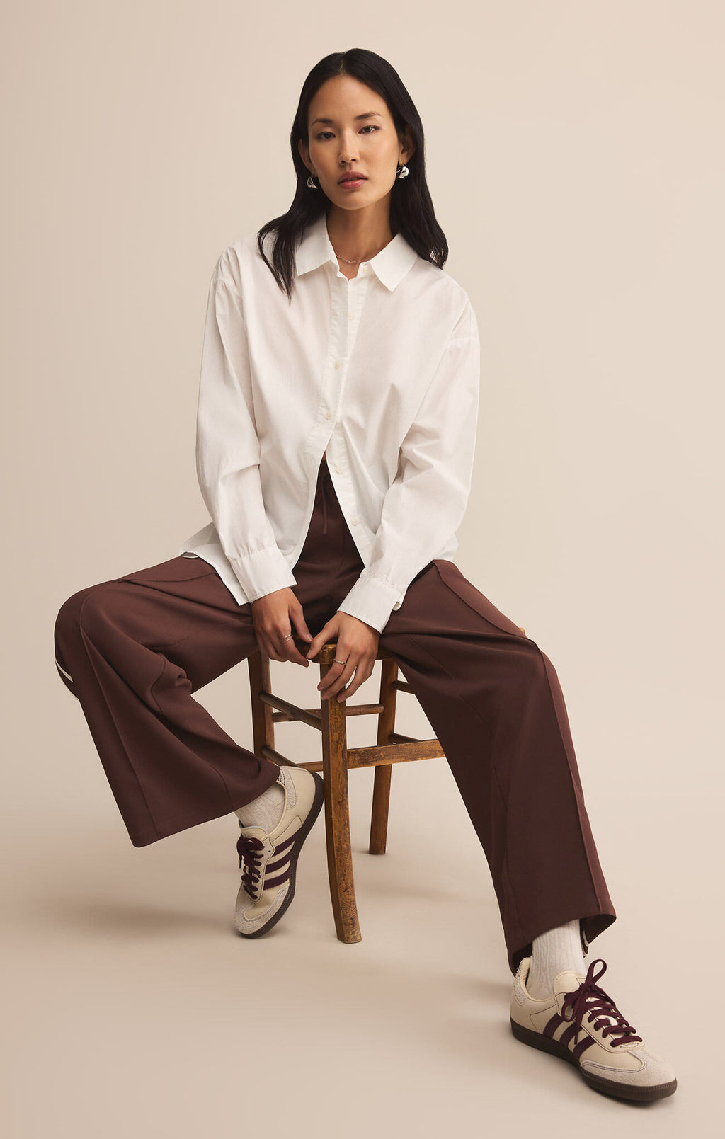 Woman sitting on a wooden stool wearing a white shirt and brown pants against a beige background
Saunder Track Pant